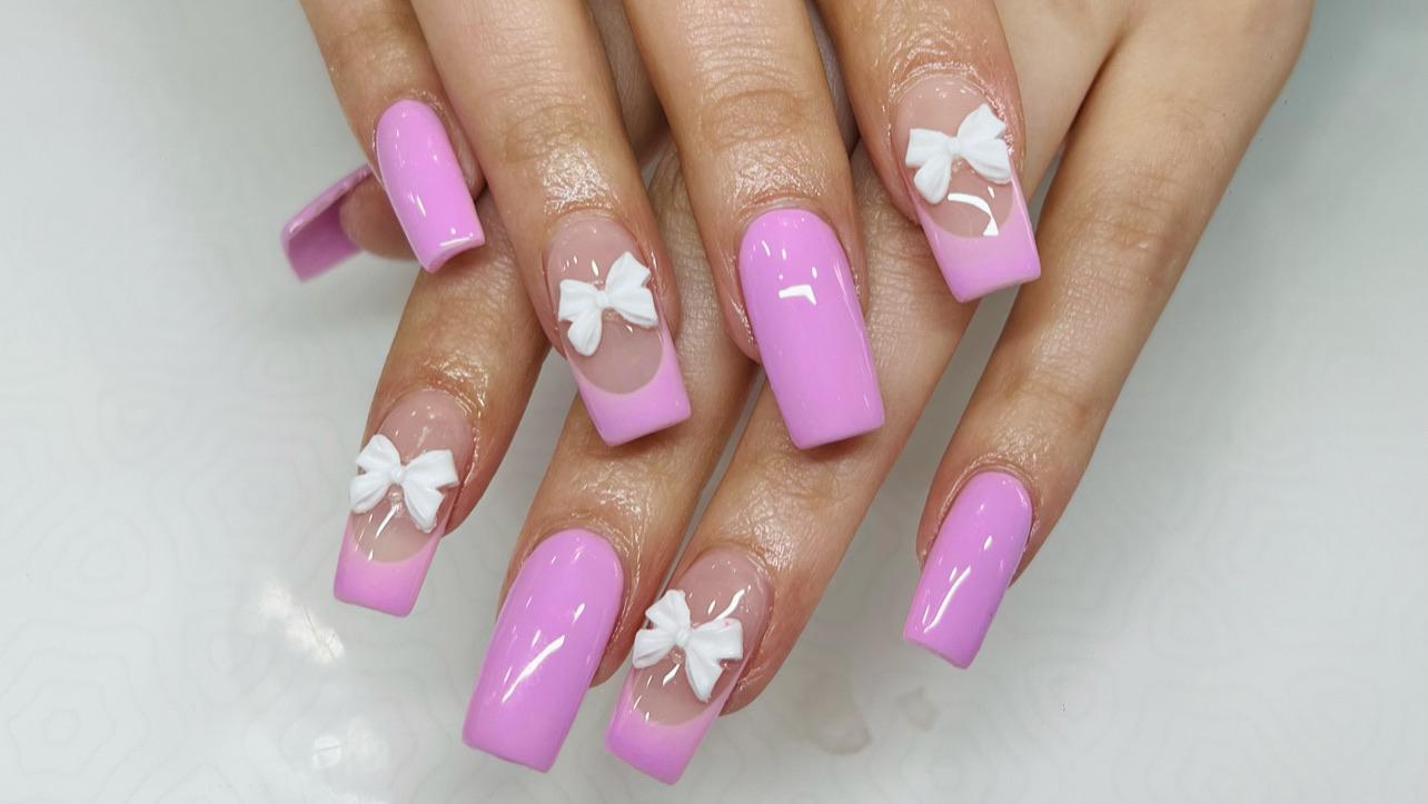 Pink acrylic nails with white 3D bow detailing, done at Lily's Nail Spa